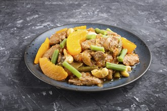 Fried pork with peaches, cashew and green beans on a black concrete background. Side view, close