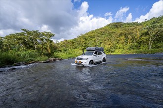 Toyota off-road vehicle with roof tent drives through a wide river in the rainforest, Alajuela