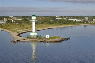 White-green lighthouse on a rocky coast with calm water and green landscape in the background,