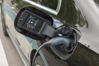 Electric car being charged at charging station, charging cable plugged into black vehicle,