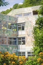 Modern building with wall art and many windows, surrounded by plants in summer, Nagold, Black