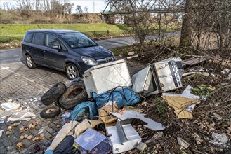 Illegal waste disposal in a car park, in a wooded area, tyres, furniture, refrigerators, household