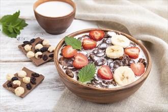 Chocolate cornflakes with milk and strawberry in wooden bowl on white wooden background and linen