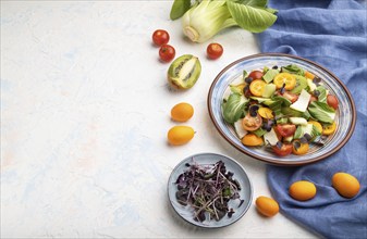 Vegetarian salad of pac choi cabbage, kiwi, tomatoes, kumquat, microgreen sprouts on a white