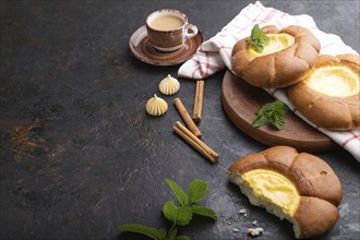 Sour cream bun with cup of coffee on a black concrete background and linen textile. Side view, copy