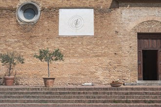 Brick wall with sundial, olive trees in pots and steps in a Mediterranean setting, Tuscany, Italy,