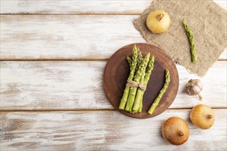 Bunch of fresh green asparagus, garlic, onion on white wooden background. Top view, flat lay, copy