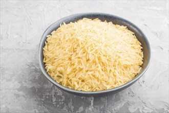 Blue ceramic bowl with raw golden rice on a gray concrete background. Side view, close up