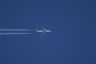 Boeing 777 aircraft of Emirates airlines flying across a blue sky leaving a contrail or vapor trail