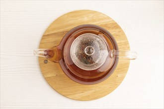 Red tea with herbs in glass teapot on white wooden background. Healthy drink concept. Top view,