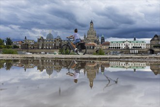 The Dresden silhouette with a cyclist and dark clouds behind the Church of Our Lady is reflected in