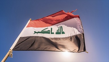 The flag of Iraq flutters in the wind, isolated against a blue sky