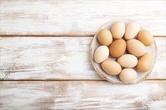 Pile of colored chicken eggs on plate on a white wooden background. top view, flat lay, copy space