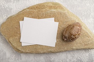 White paper business card, mockup with natural stone and seashell on gray concrete background.