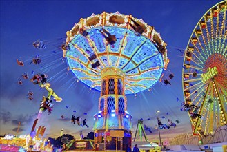 The colourfully illuminated Wellenflug chain carousel and the Ferris wheel in the evening, Cranger