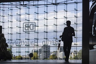 Central station, travellers in front of the glass facade with the logo of Deutsche Bahn AG. Berlin,