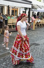 Woman in traditional dress eating ice cream on a busy street, child in the background, young woman