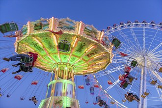 Illuminated chain carousel and Ferris wheel at night with cheerful people, funfair, wave flight,