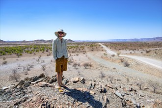 Young man standing on a hill, barren dry landscape with hills, Damaraland, Kunene, Namibia, Africa