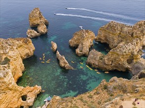 Rocky coast with turquoise-coloured water, kayaks and small boats. Impressive rock formations and