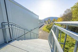 Stairwell of a container building with view of sunny landscape and railing, refugee accommodation