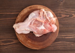 Raw turkey wing on a wooden cutting board on a brown wooden background. Top view, close up