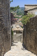 Stony alley in a village with views of houses and countryside in the distance, Vaison-la-Romaine,