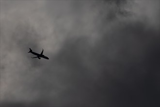 Airbus A321 jet passenger aircraft flying under dark clouds in the sky, England, United Kingdom,