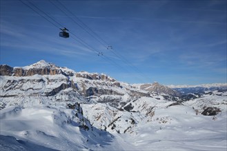 View of a ski resort piste with people skiing in Dolomites in Italy with cable car ski lift. Ski