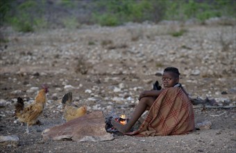 Young shepherdess from the Himba people sitting by a campfire, Ombombo, Kaokoland, Kunene, Namibia,