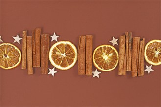 Seasonal natural dried orange slices, cinnamon sticks and star ornaments in a row on brown