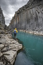 Tourist standing by the river in Stuðlagil Canyon, turquoise blue river between basalt columns,