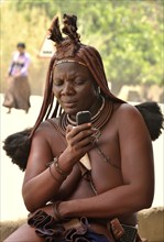 Himba woman in traditional costume typing on her mobile phone, Opuwo, Kaokoland, Kunene, Namibia,