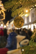 A decorative pendant on a fir branch at a busy Christmas market at night, Christmas market, Nagold,