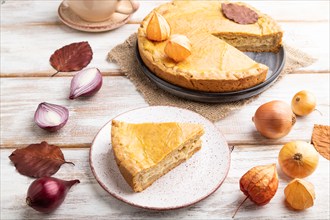 Autumn onion pie and cup of coffee on white wooden background and linen textile. Side view, close