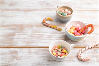 Heap of multicolored caramel candies in cups on white wooden background. copy space, side view,