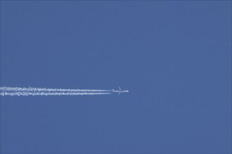 Airbus jet passenger aircraft flying in a blue sky with a vapor trail or contrail behind, England,