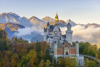 Neuschwanstein Castle in front of mountains in the fog, surrounded by autumnal trees, Schwangau,