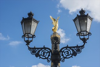 Victory Column behind a beautiful, old street lamp in a blue sky with white clouds, towering column