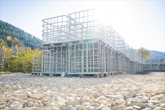 Stacked metal cages outdoors on a gravelled area in a sunny landscape, refugee accommodation