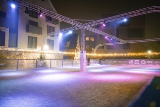 Empty ice rink with colourful lights in a modern architectural setting at night, Christmas market,