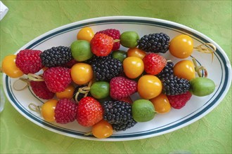 Fruit skewers arranged on serving platter, raspberries, blackberries, kiwi, physalis, bladder