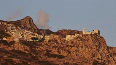 Mountain village in warm morning light with striking rock formations and clouds, Mountain village