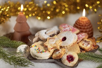 Various Christmas biscuits on a plate, surrounded by candles and decorations