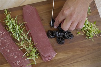 Swabian cuisine, preparation of lamb with prunes, raw lamb, rosemary, herbs, sliced garlic, lemon