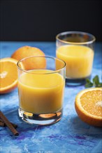 Glass of orange juice on a black and blue background. Hard light, contrast. Side view, close up