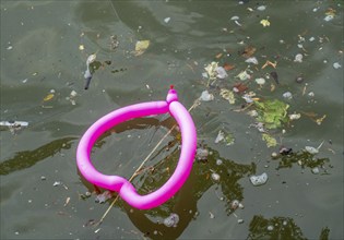 Pink balloon, shaped like a heart, floats in a dirty river