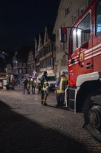 Night shot of a fire engine in front of half-timbered buildings with emergency services in the