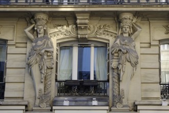 Two stone caryatids frame a window in the façade of a house in Paris as a decorative element.