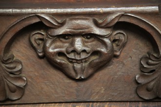 Wooden carved devil face in bench seat, Ufford church, Suffolk, England, UK